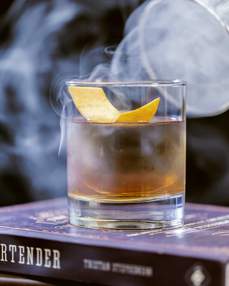 Old Fashioned cocktail with an orange peel garnish and smoke